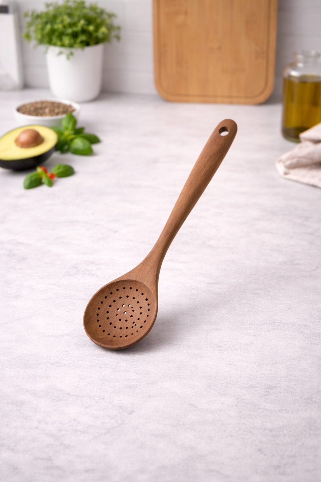 Wooden cooking spoon on a kitchen counter with an avocado and cutting board in the background.