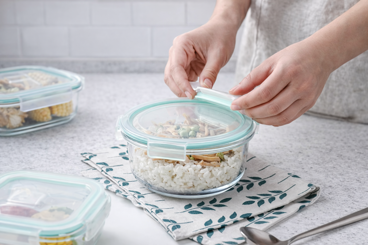 Person sealing a glass food container with a lid on a kitchen counter.