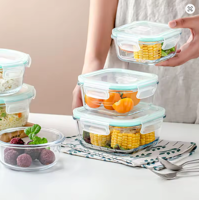 Glass food storage containers with lids on a table, filled with fruits and vegetables.
