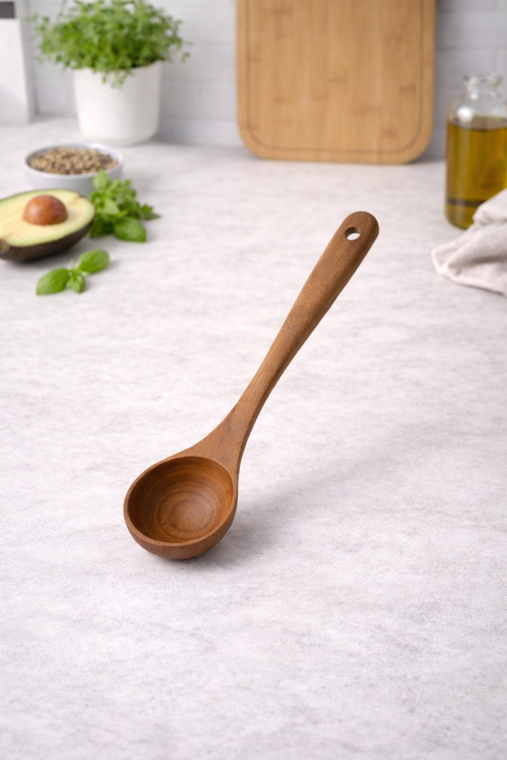 Wooden spoon on a kitchen counter with an avocado, herbs, and a cutting board in the background.